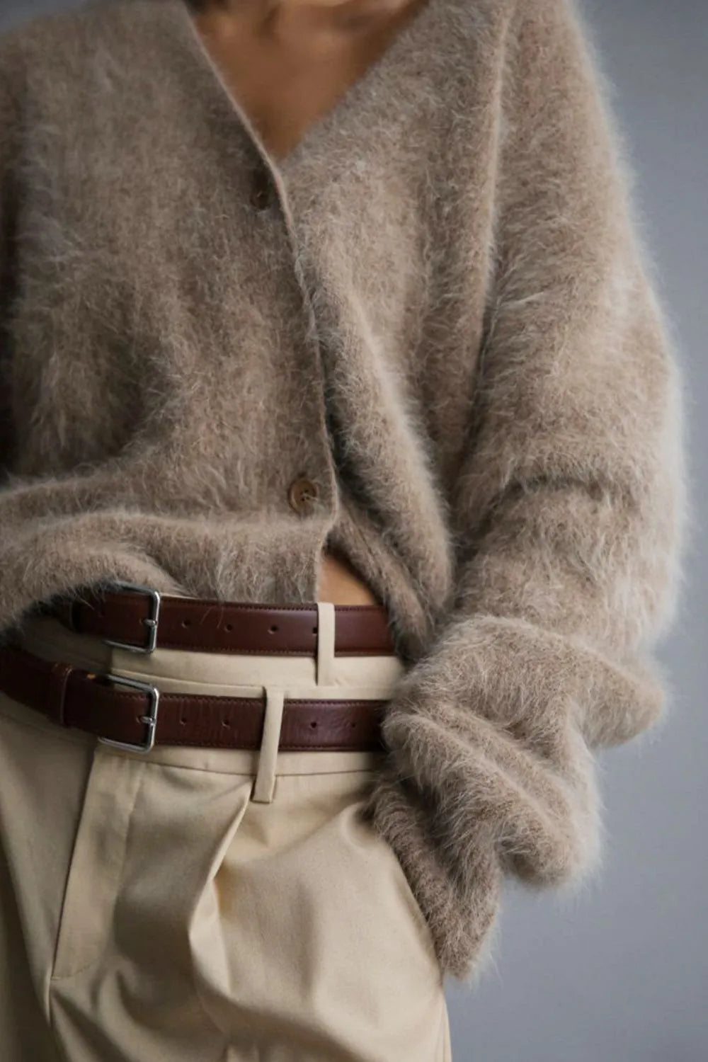 Person wearing a fluffy beige cardigan and beige pants with a belt, on a plain background