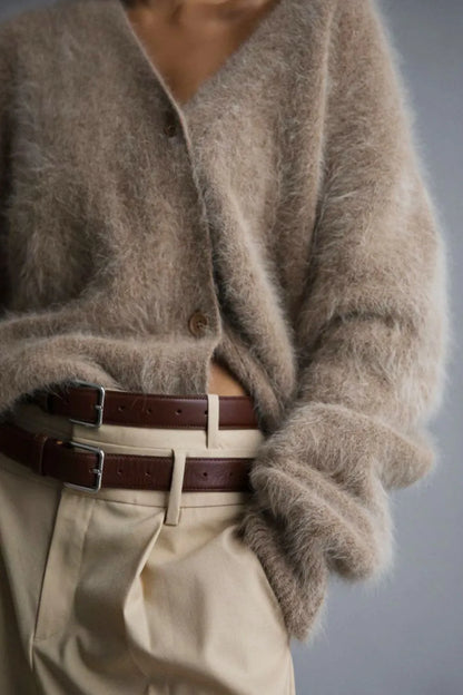 Person wearing a fluffy beige cardigan and beige pants with a belt, on a plain background