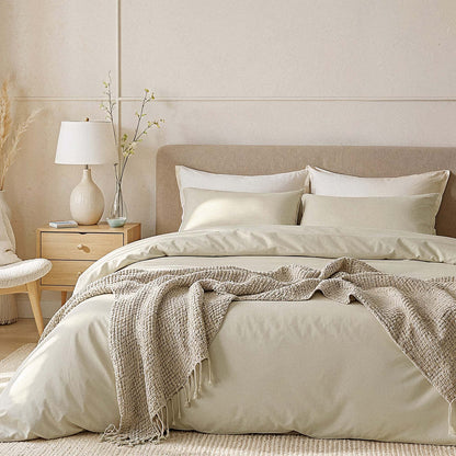 Neatly made bed with beige bedding and a lamp on a nightstand in a bedroom.