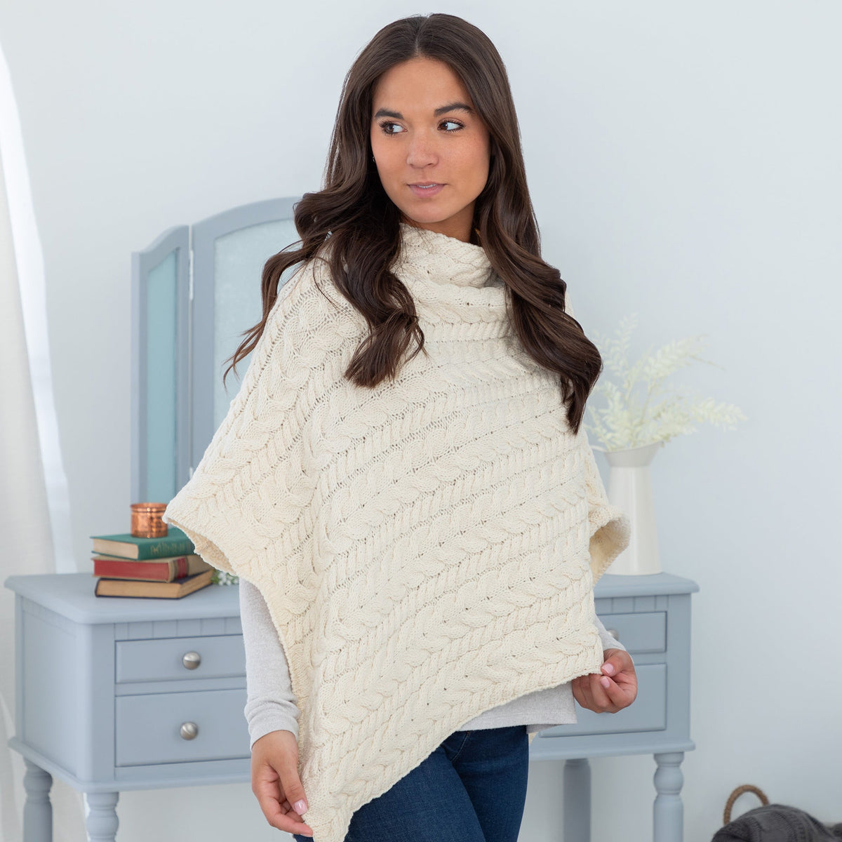 Woman wearing a cream-colored knitted poncho in a room with light blue walls and furniture.