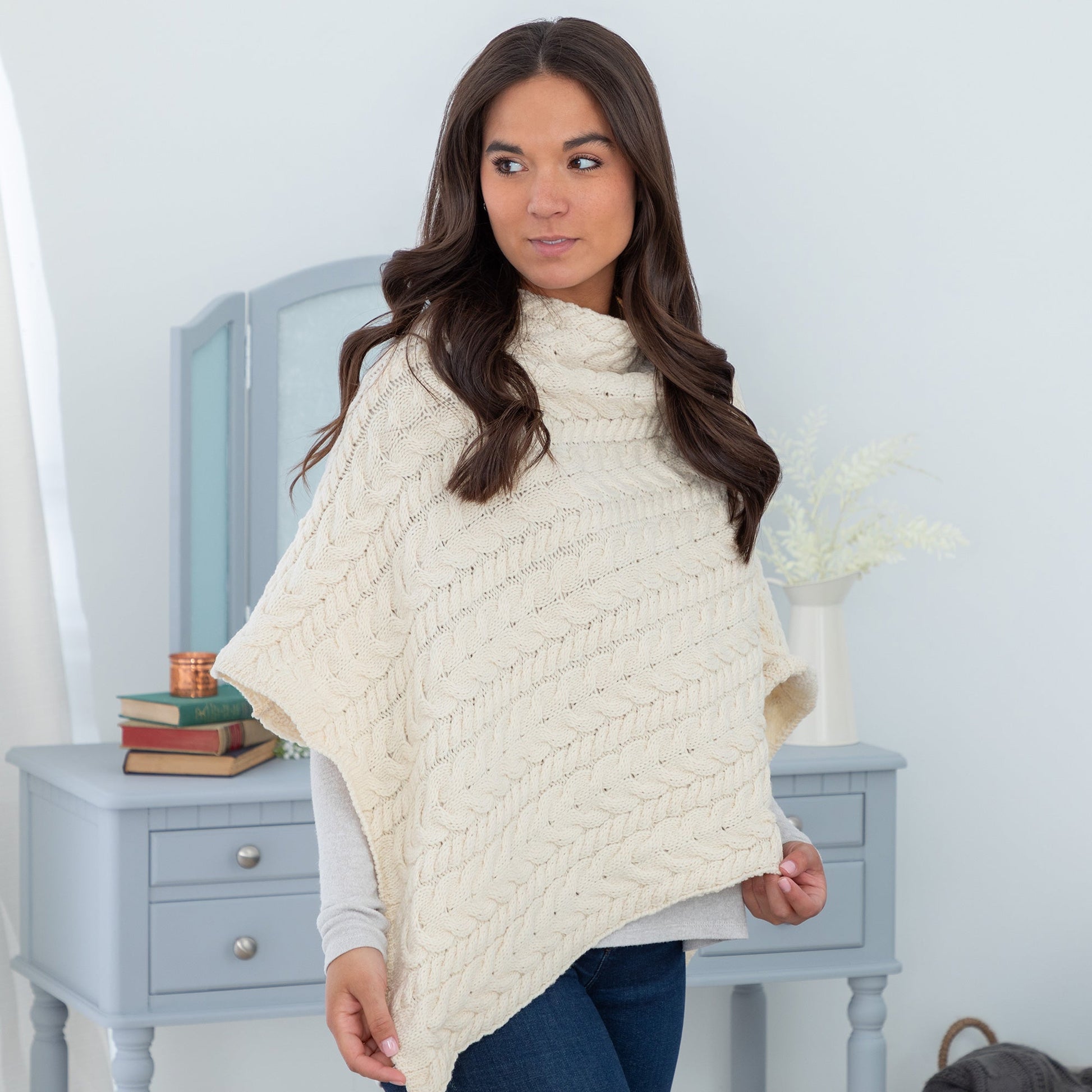 Woman wearing a cream-colored knitted poncho in a room with light blue walls and furniture.