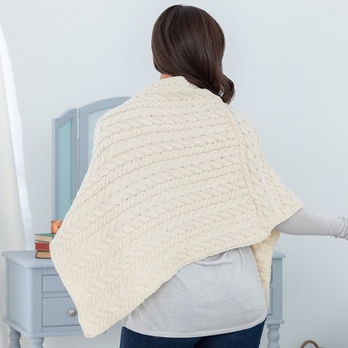 Back view of a woman wearing a cable knit wool poncho in cream color.