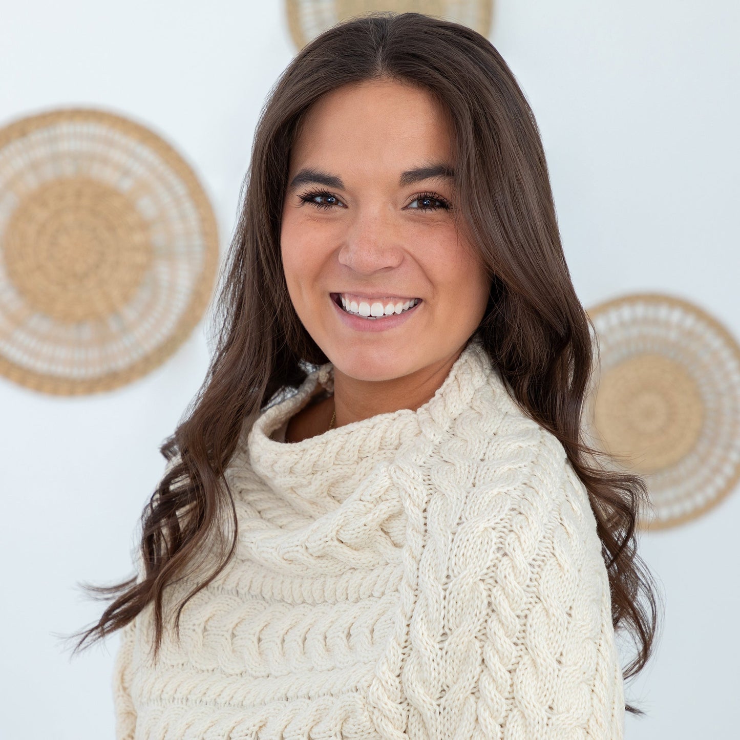 Woman wearing a cream cable knit sweater with decorative plates in the background