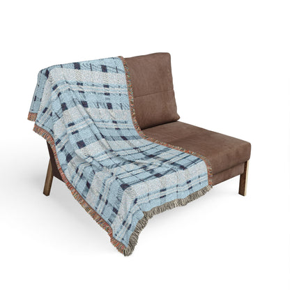 A brown upholstered lounge chair with a light blue, gray, and navy plaid throw blanket draped over it, shown on a plain white background.
