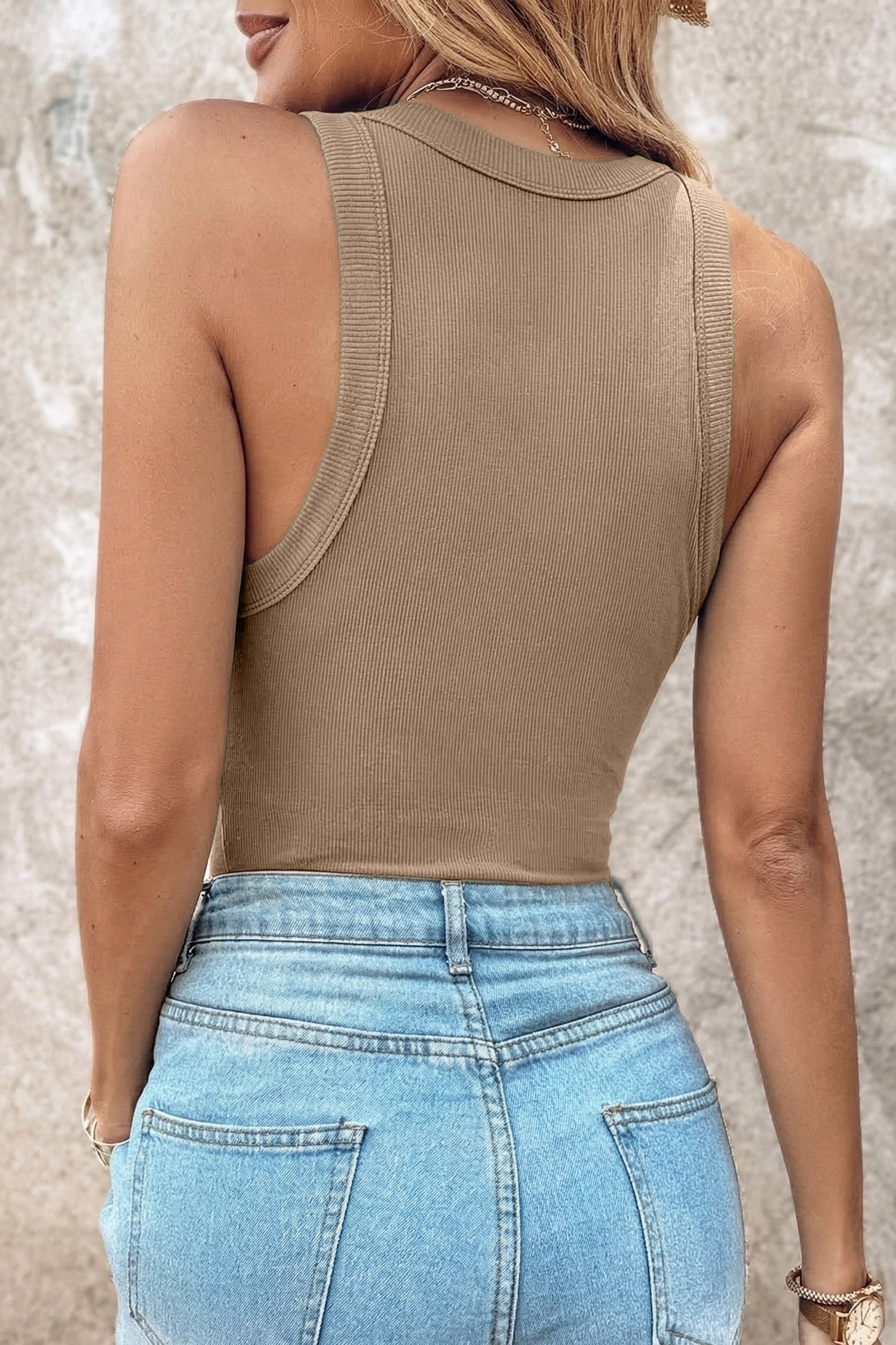 Rear view of a person wearing a tan ribbed fabric tank top tucked into light blue denim pants.