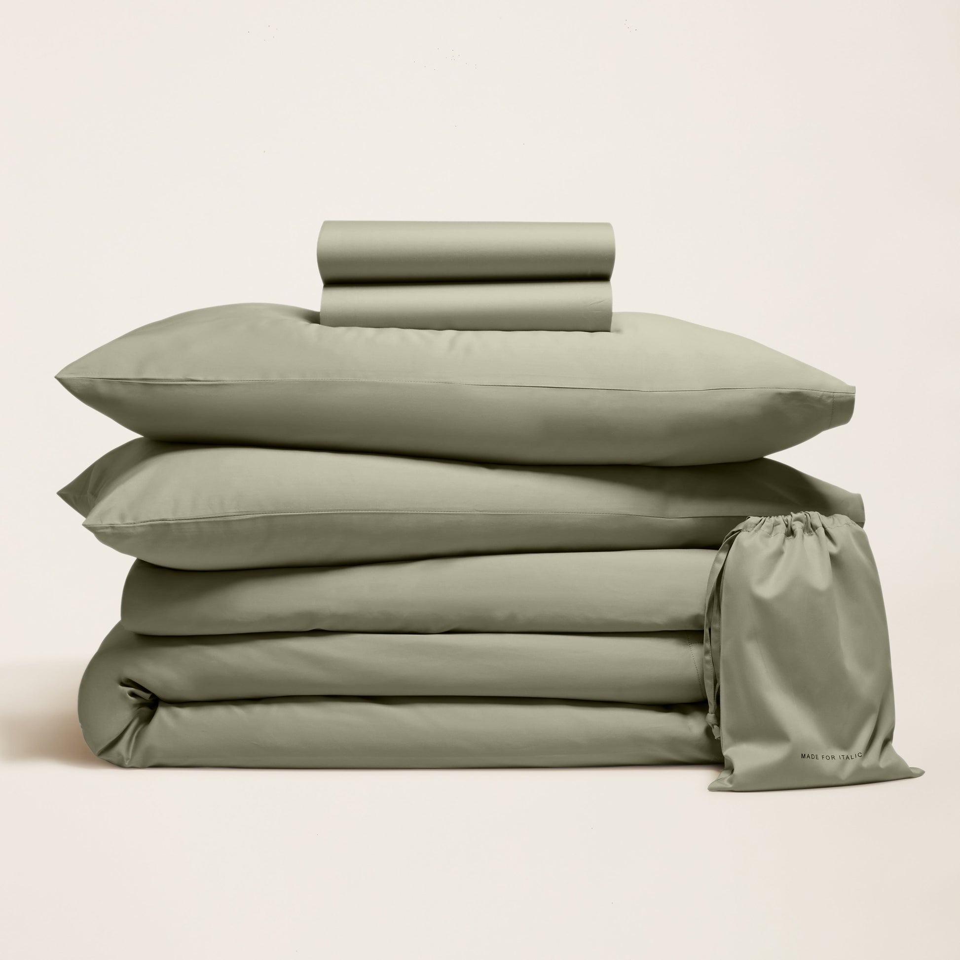 Green bedding set with duvet, pillowcases, and drawstring bag on a beige background