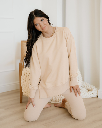 Woman in beige outfit sitting on the floor with a white background