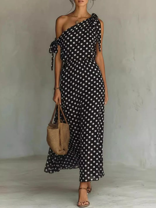 Woman wearing a black polka dot dress holding a woven bag against a plain background