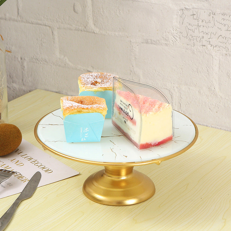 Three small cakes on a marble stand with a gold base, against a light gray brick wall.