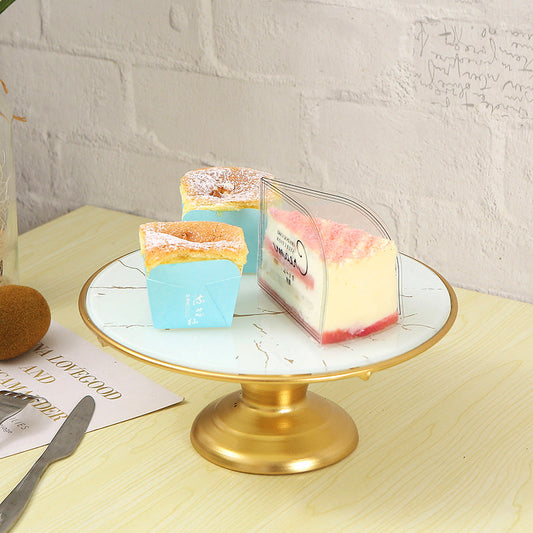 Three small cakes on a marble stand with a gold base, against a light gray brick wall.