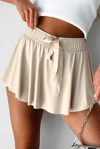 Beige fabric tennis skort with an elastic drawstring waistband and flared hem.
