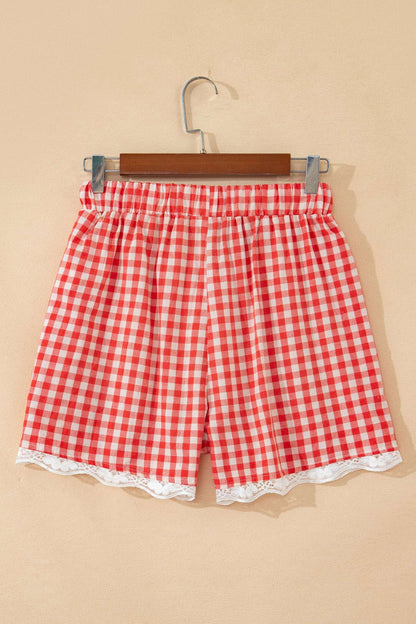 Red and white gingham fabric shorts with an elastic waist and white lace trim at the hem, hanging on a wooden clip hanger.