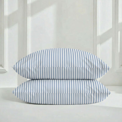 Two blue and white striped pillows on a white surface with a light wooden panel background.
