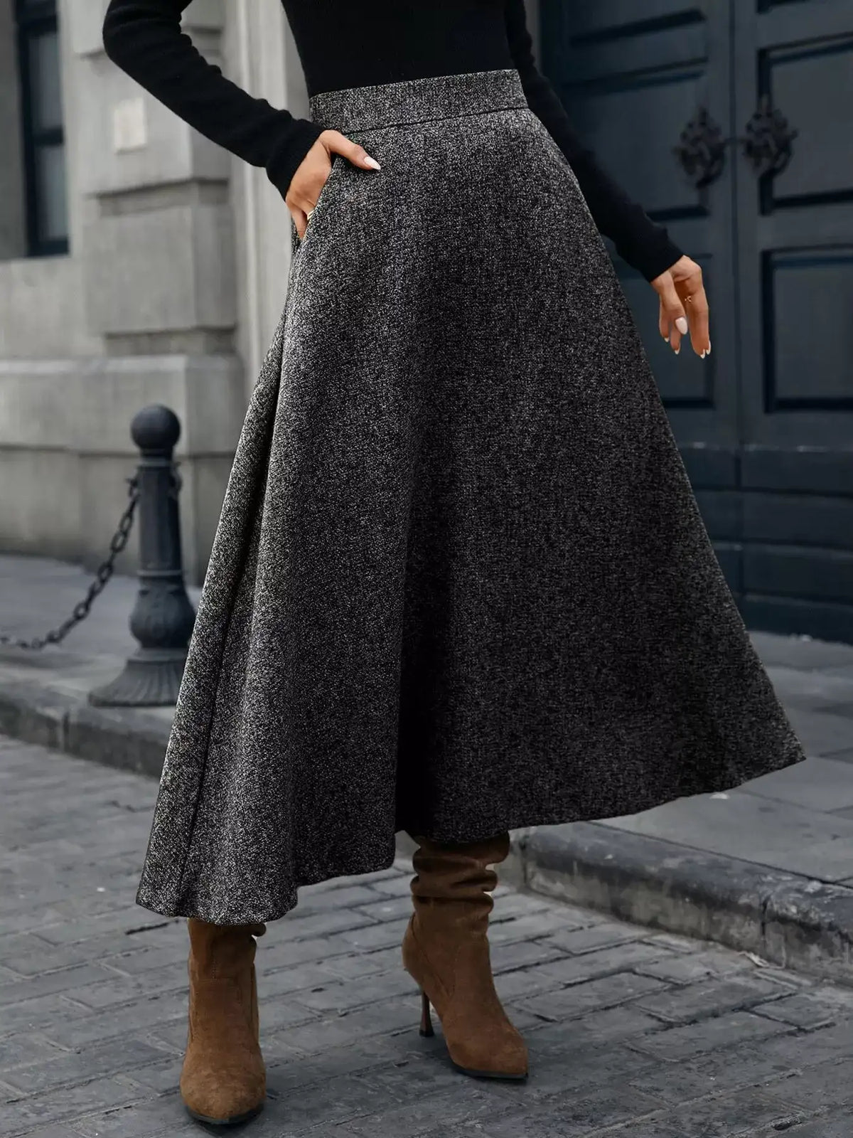 Person wearing a long dark gray skirt and brown boots on a city street.