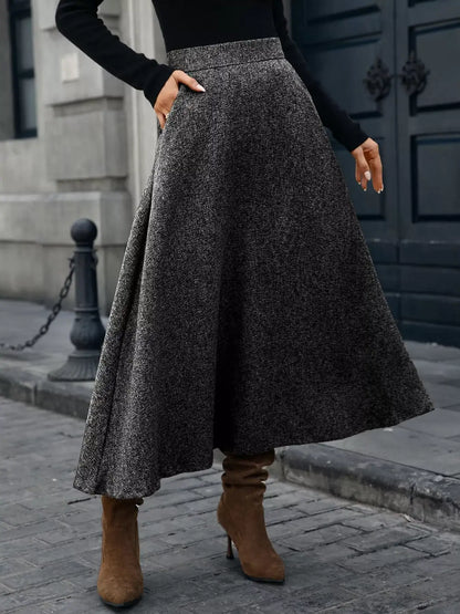 Person wearing a long dark gray skirt and brown boots on a city street.