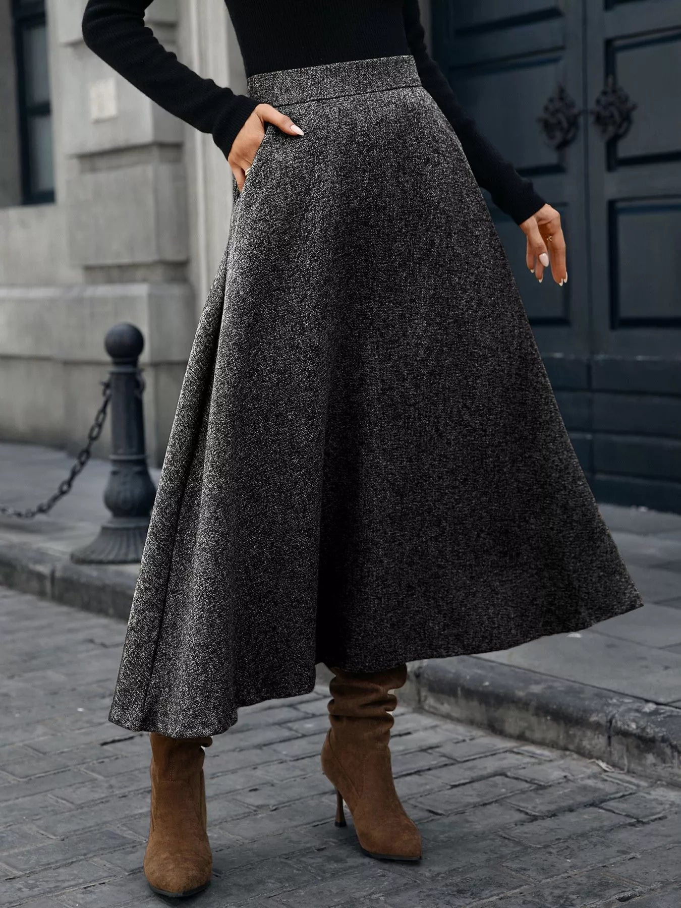 Person wearing a long dark gray skirt and brown boots on a city street.