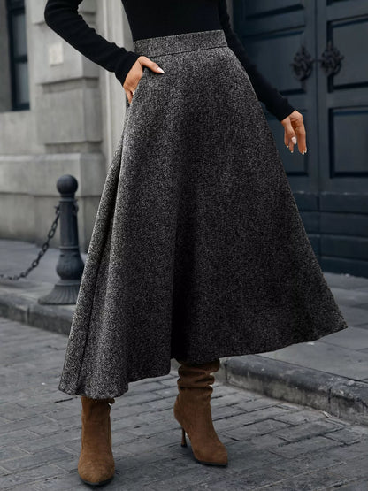 Person wearing a long dark gray skirt and brown boots on a city street.