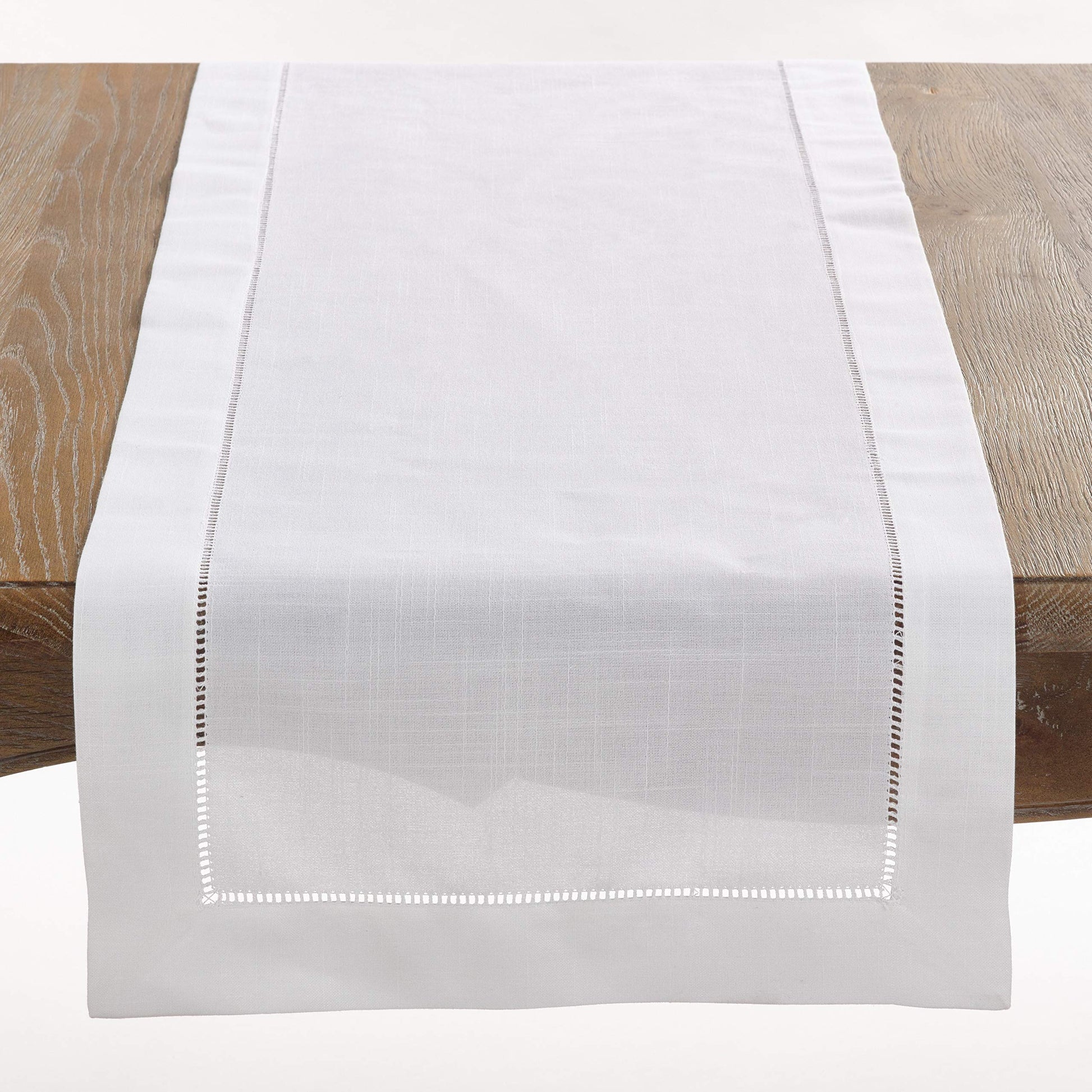 A white woven table runner with delicate embroidered borders, displayed on a rustic wooden table.