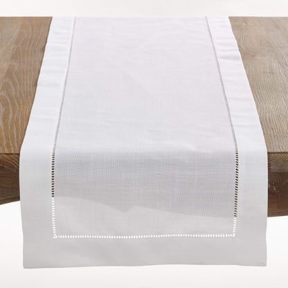 A white woven table runner with delicate embroidered borders, displayed on a rustic wooden table.
