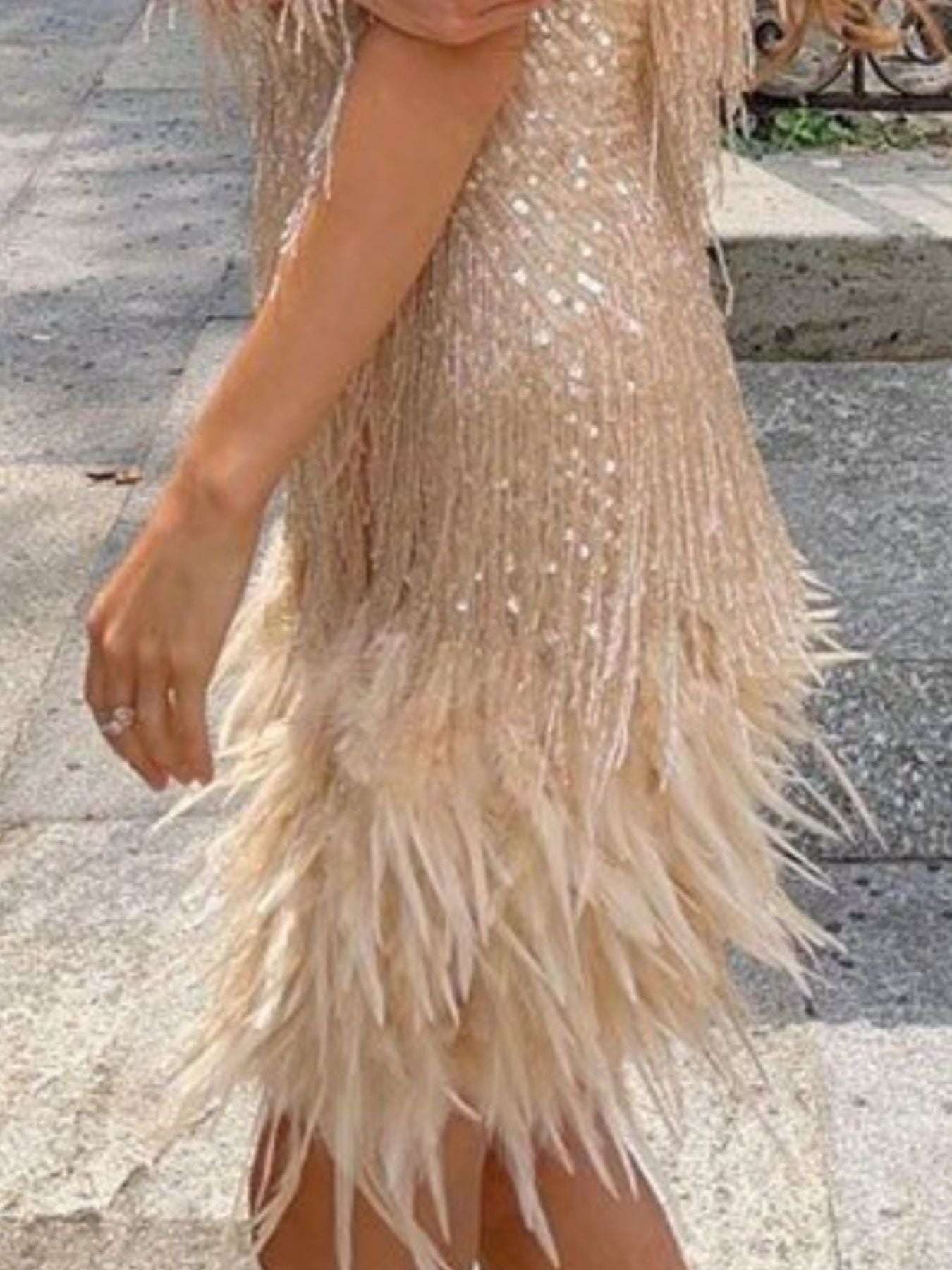 Beige sequin dress with feather details on a stone pavement background