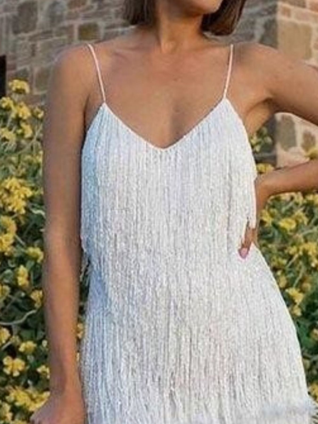Woman wearing a white lace dress with a blurred background of greenery and a stone wall.