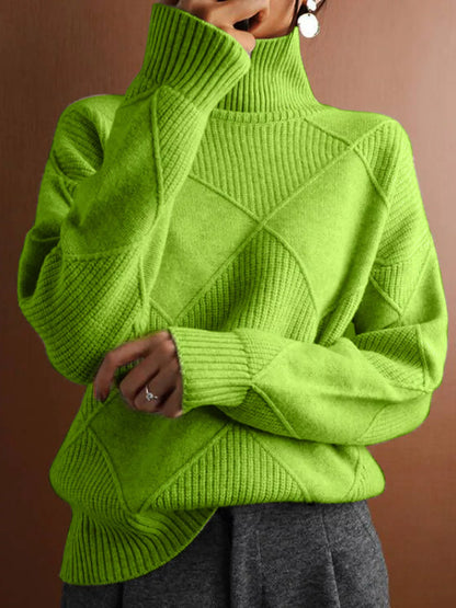 A person wearing a bright lime green ribbed turtleneck sweater with diamond-shaped knit patterns on the front, paired with gray pants, against a solid brown background.