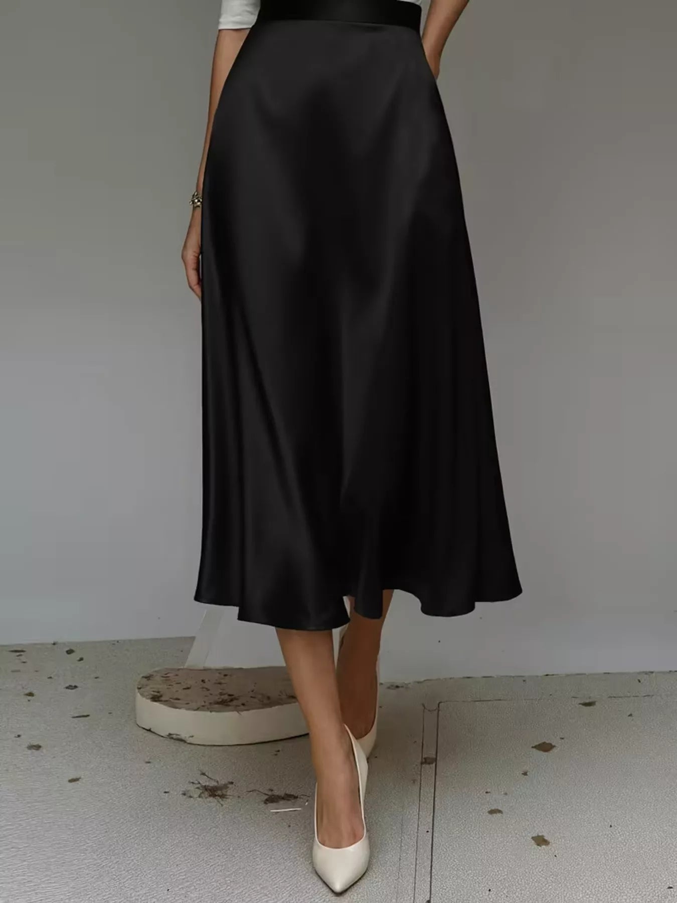 Person wearing a black satin skirt with white shoes on a plain background