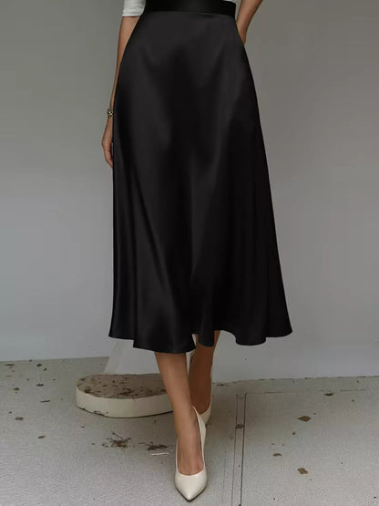 Person wearing a black satin skirt with white shoes on a plain background