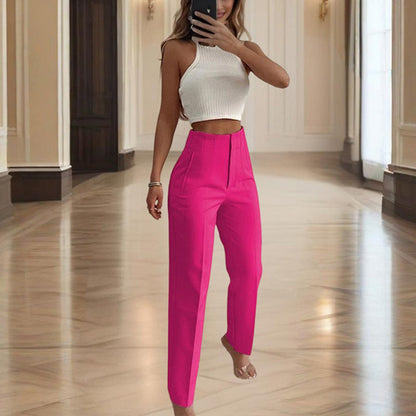 Woman taking a mirror selfie wearing a white top and bright pink pants in an elegant hallway.