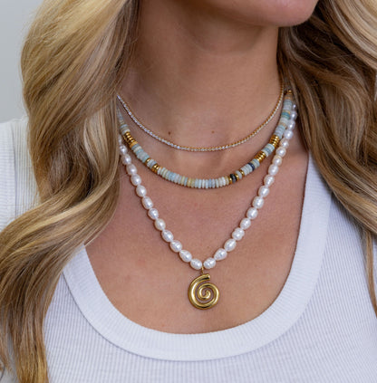 Close-up of a woman wearing multiple necklaces with a plain background