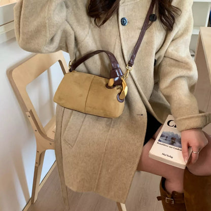 Person holding a beige handbag and a book, wearing a beige coat indoors.