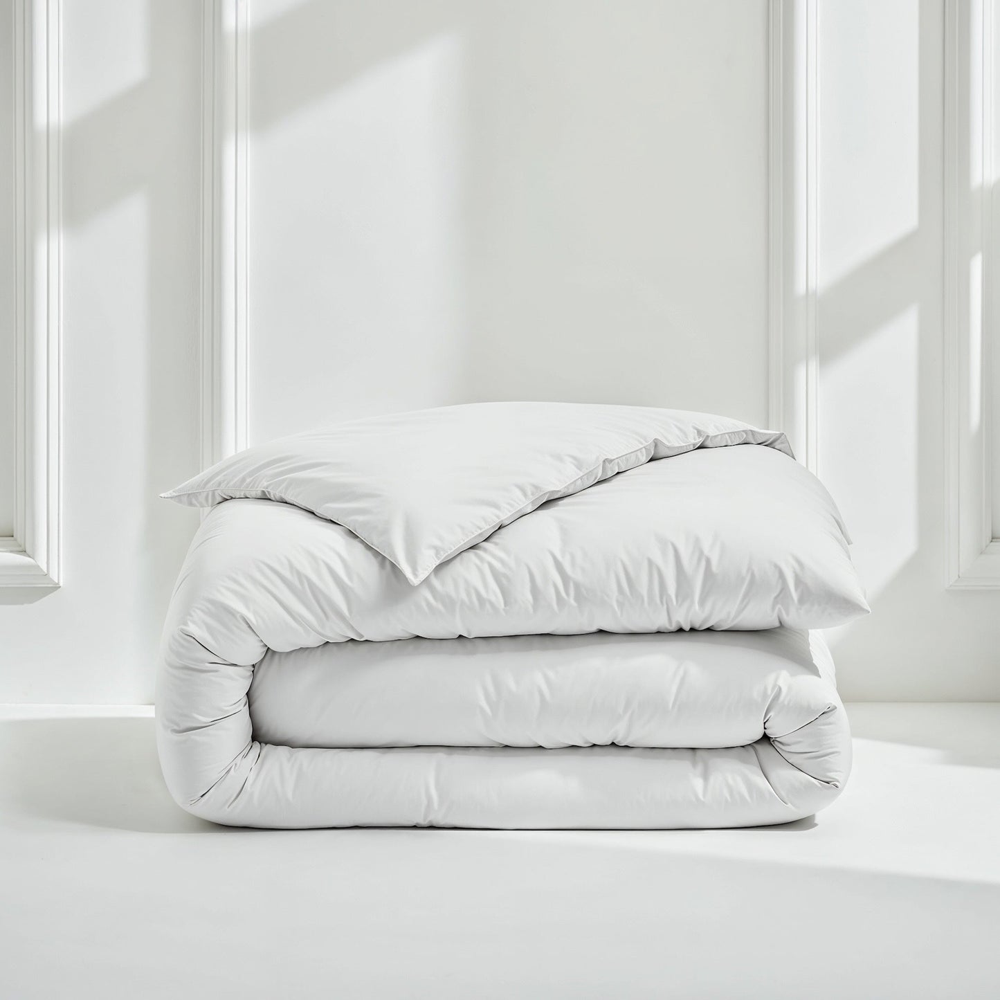 Folded light gray comforter on a white surface with a neutral background