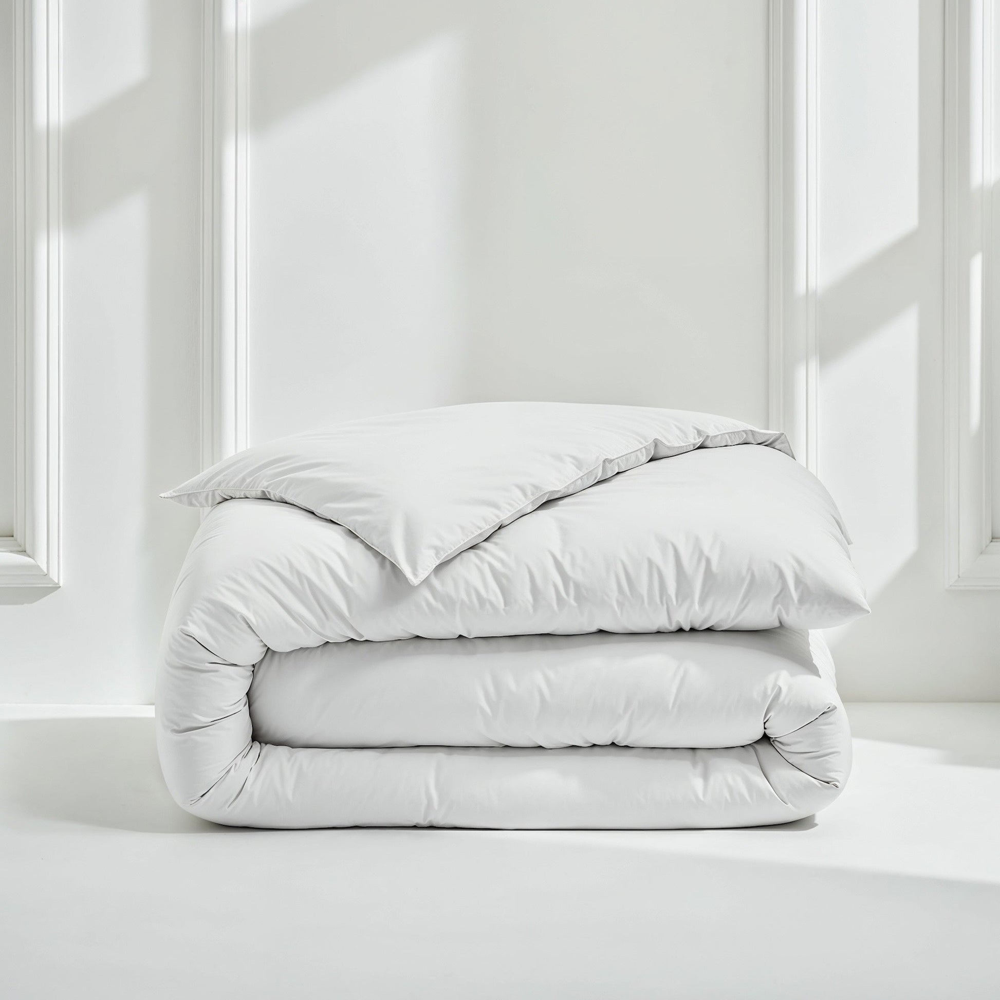 Folded light gray comforter on a white surface with a neutral background