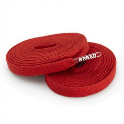 Two coiled red fabric shoelaces with clear plastic tips featuring the white BREAD logo.