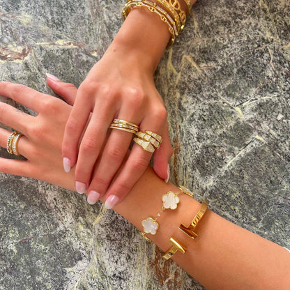 Two hands with gold jewelry on a stone surface