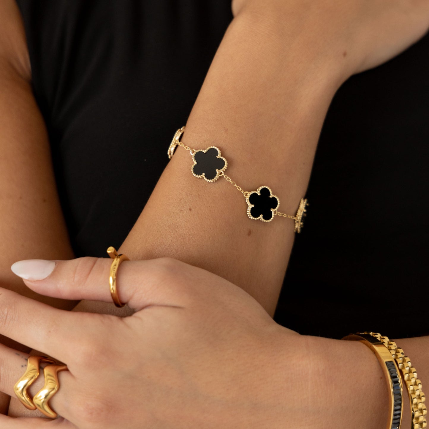 Close-up of a wrist wearing a gold bracelet with clover-shaped charms against a black background.