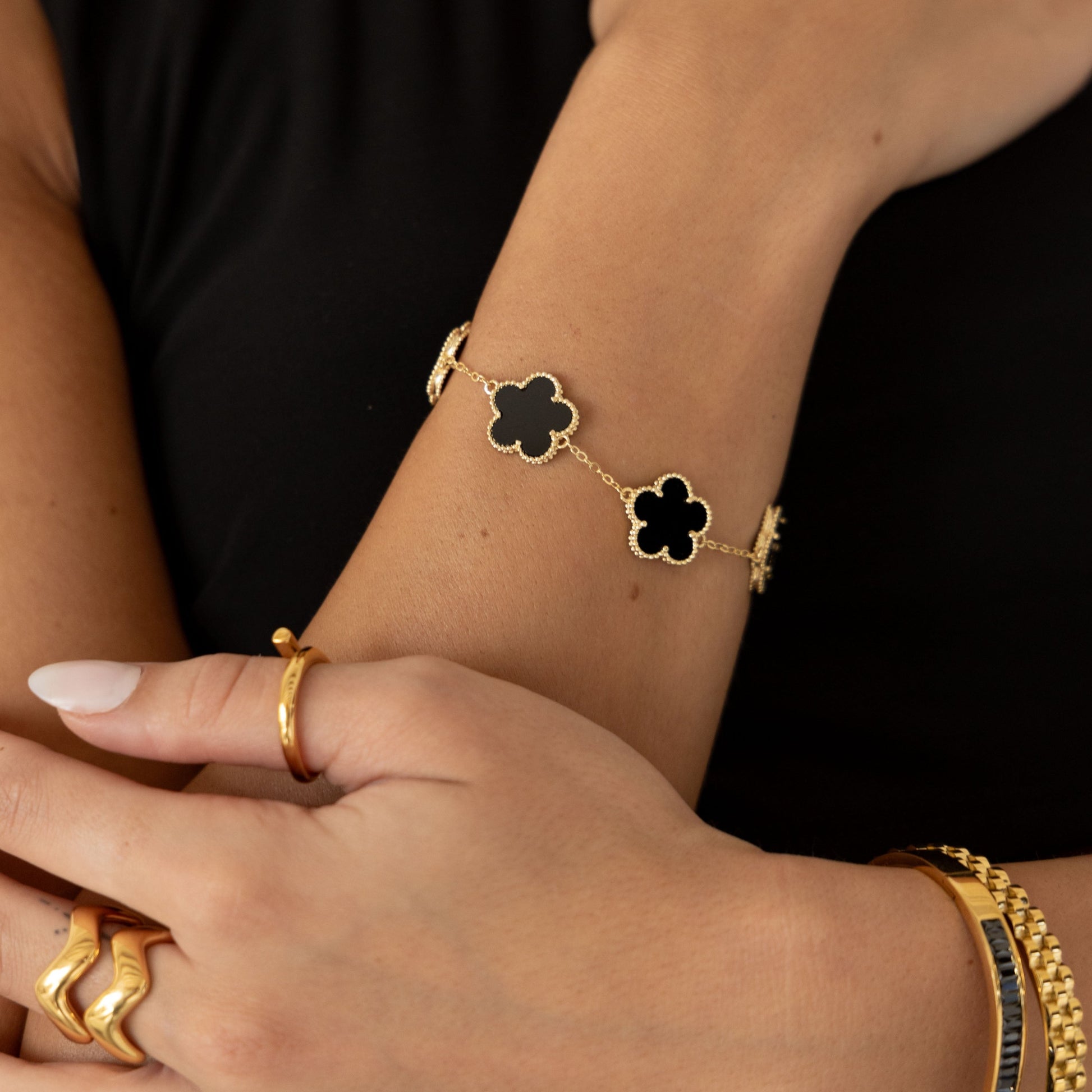 Close-up of a wrist wearing a gold bracelet with clover-shaped charms against a black background.