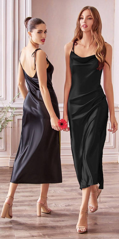Two women wearing black satin slip dresses in a room with wooden flooring and white walls.
