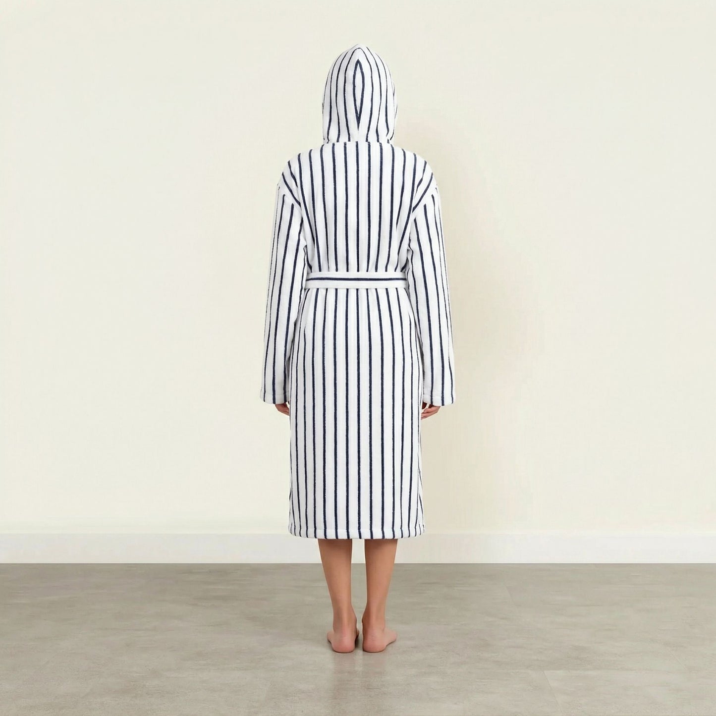Person wearing a black and white striped robe with a hood in a minimalistic setting.