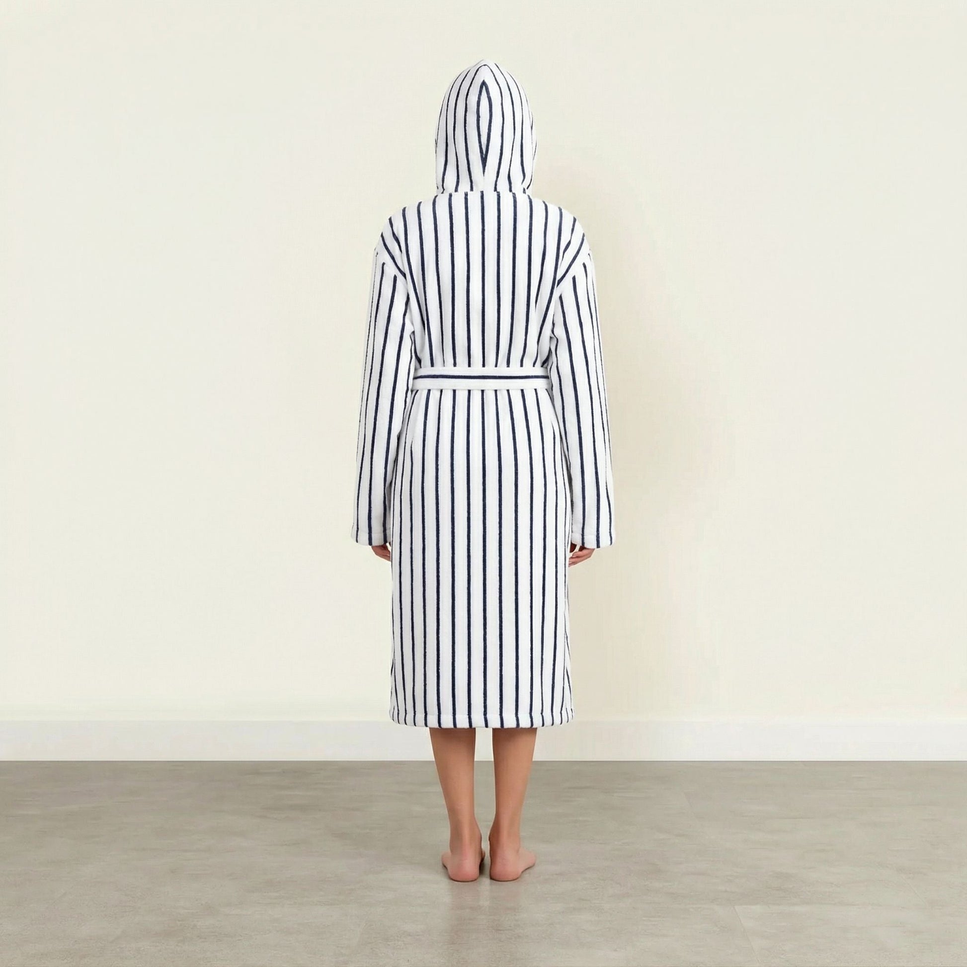 Person wearing a black and white striped robe with a hood in a minimalistic setting.