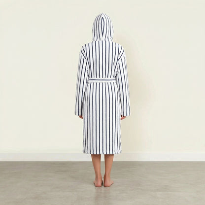 Person wearing a black and white striped robe with a hood in a minimalistic setting.