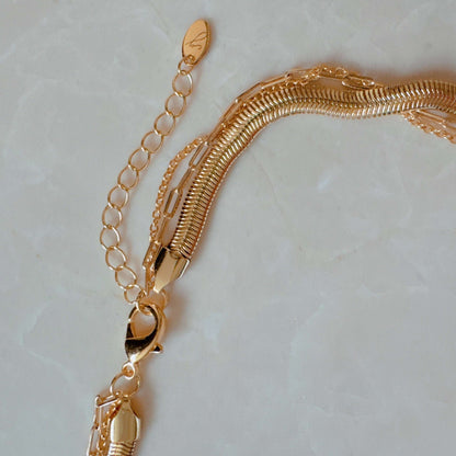 Close-up of a gold metal layered necklace featuring a thick snake chain, thin link chains, and a lobster claw clasp.