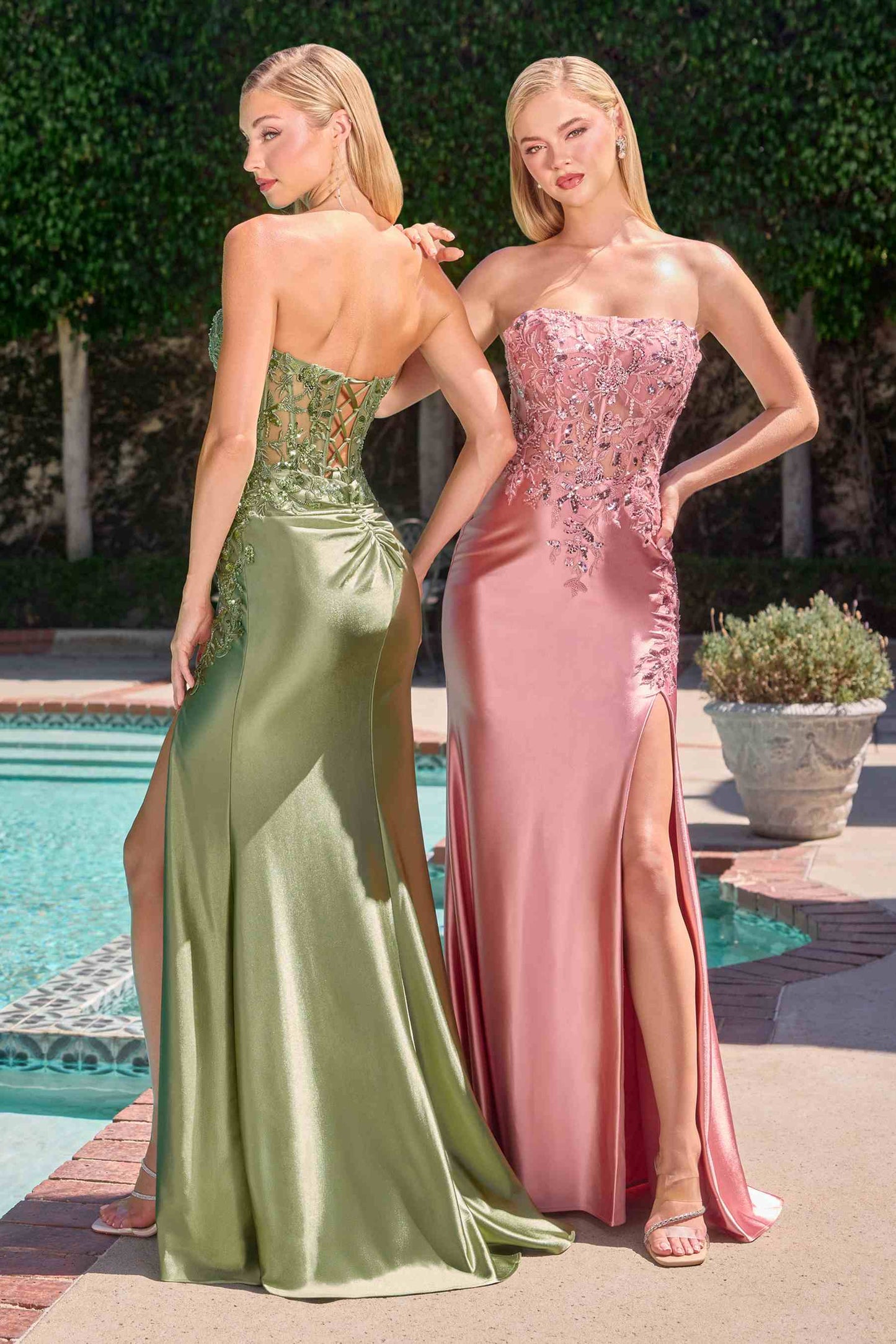 Two women in formal evening gowns standing by a poolside.