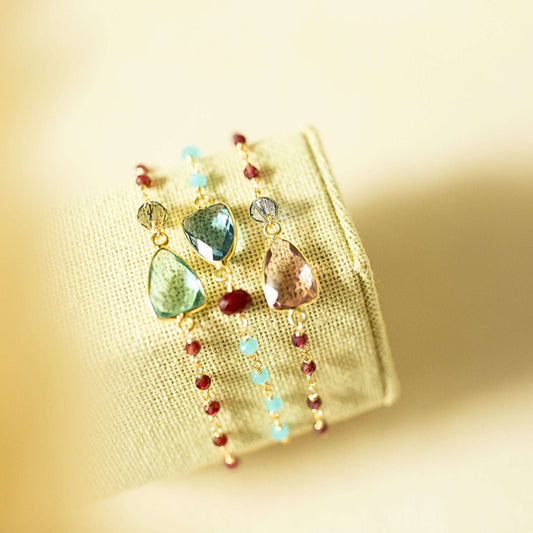 Colorful earrings with gemstones on a textured beige background