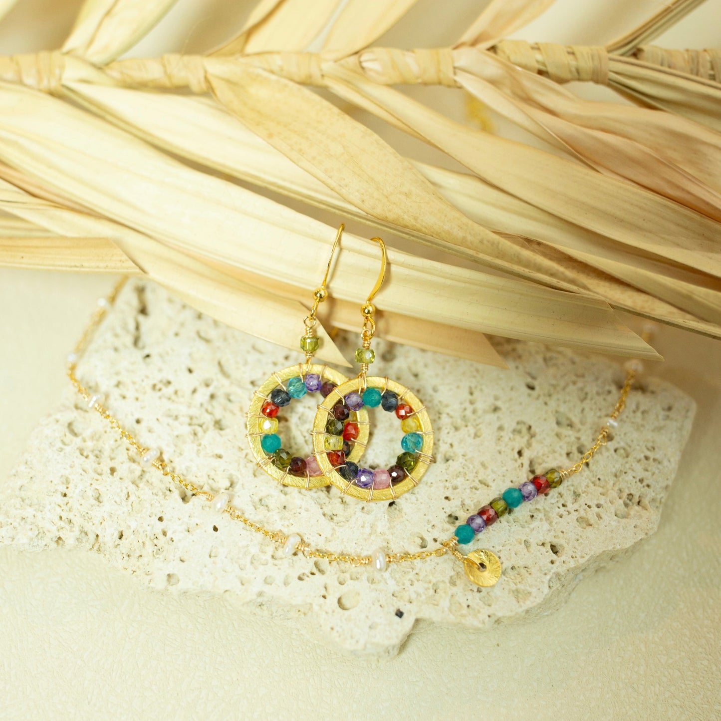 Gold earrings with colorful beads on a textured surface with dried leaves