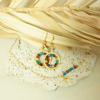 Gold earrings with colorful beads on a textured surface with dried leaves