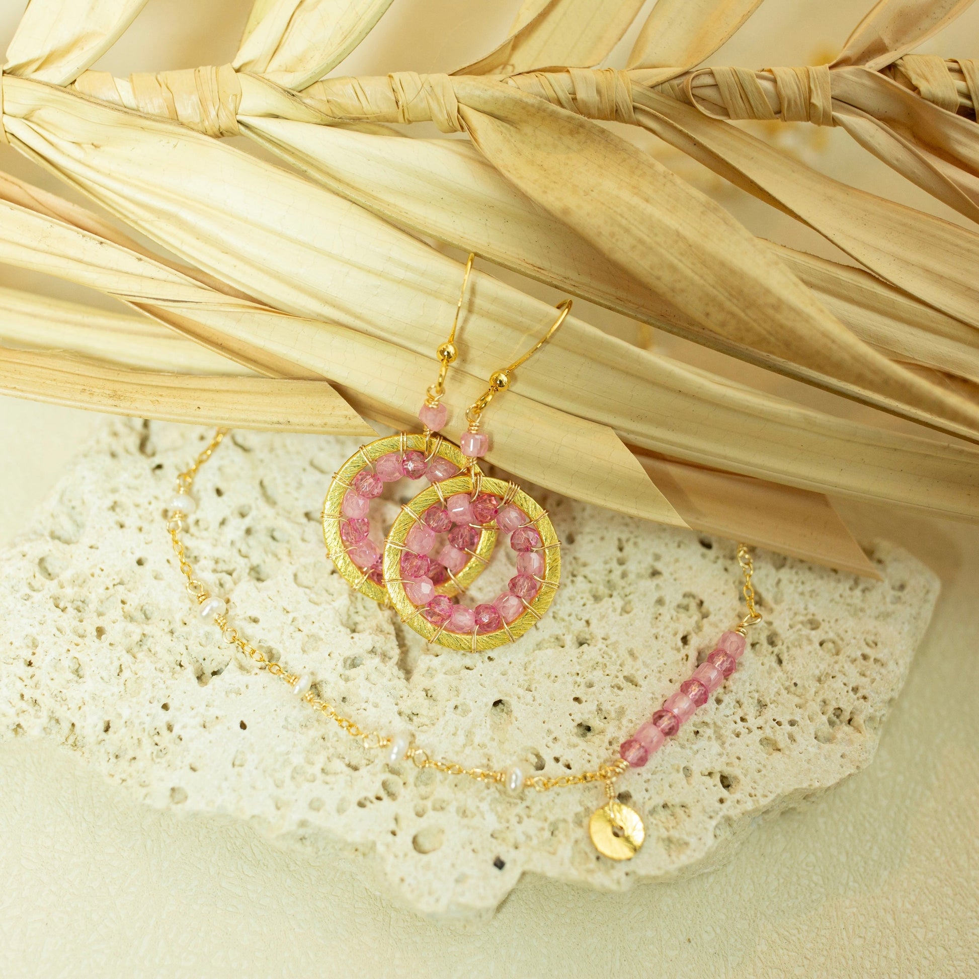 Gold and pink jewelry set on a textured surface with dried leaves