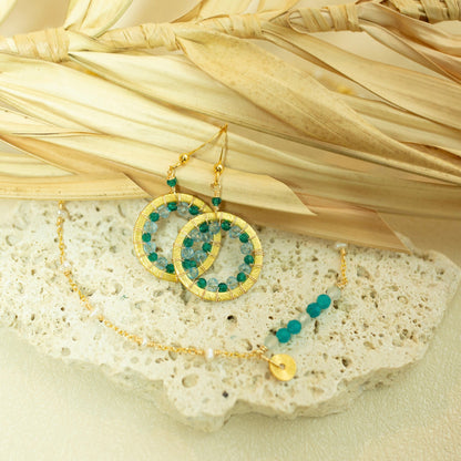 Gold and green beaded jewelry set on a stone surface with straw background