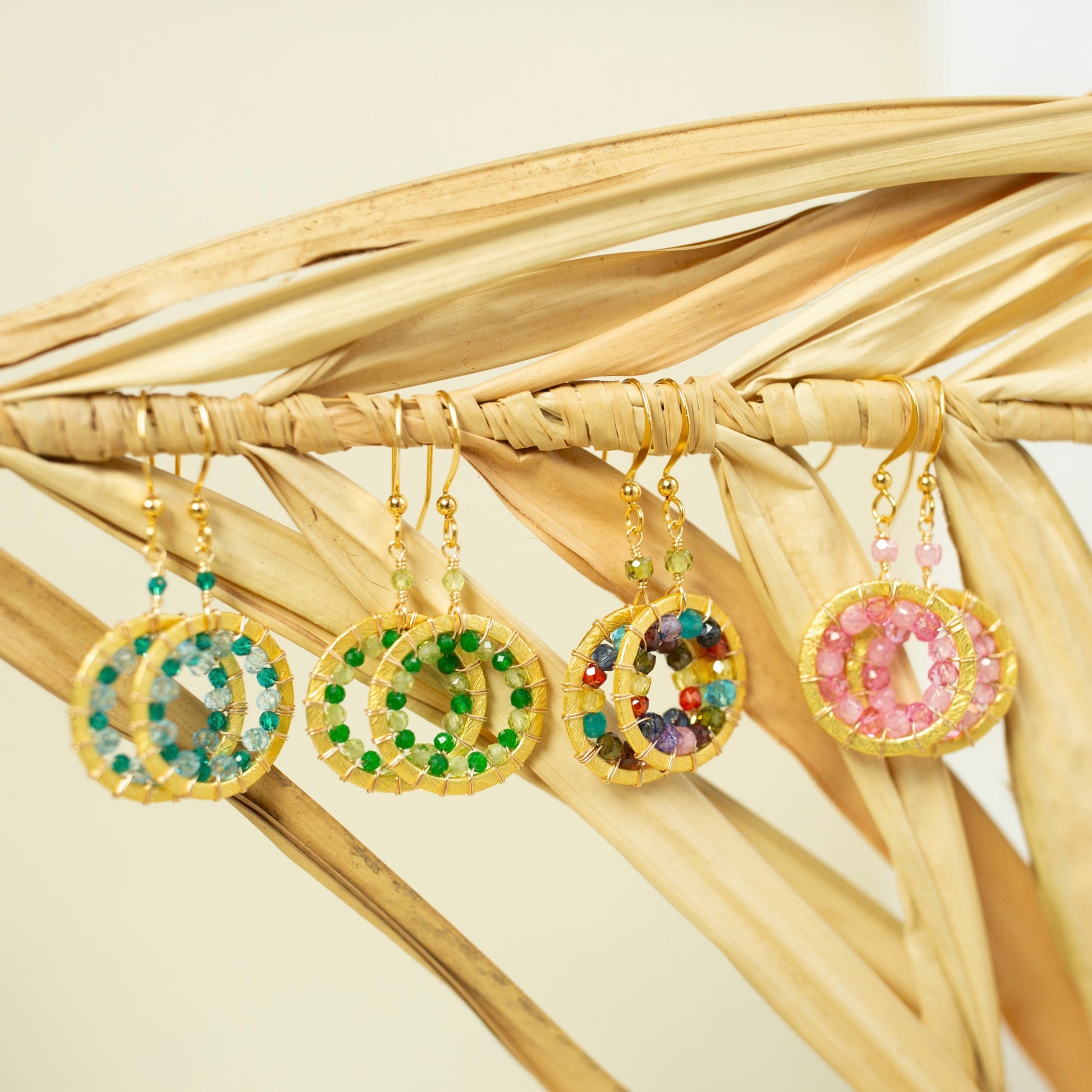 Four colorful beaded earrings on a woven surface with a neutral background