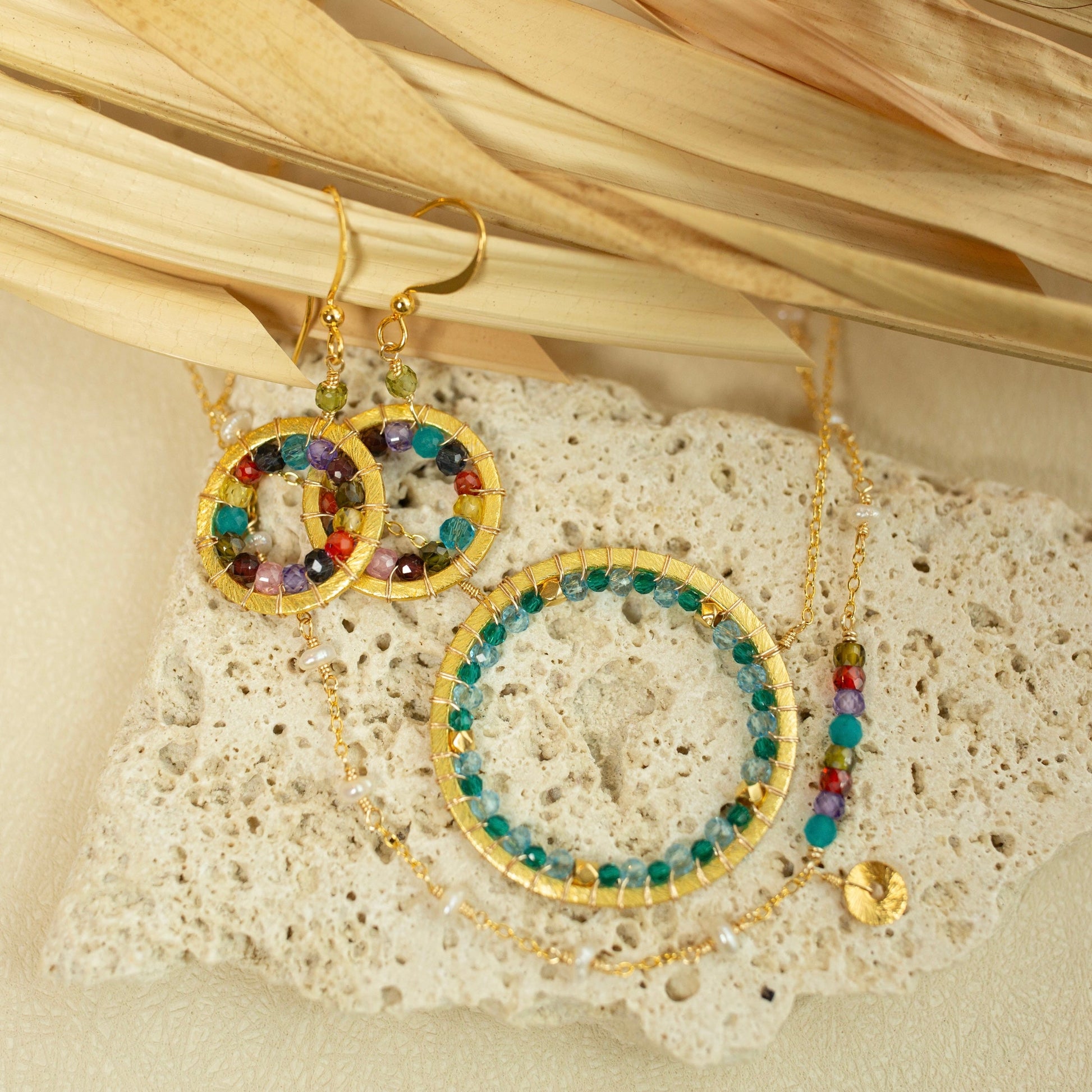 Gold hoop earrings with colorful beads on a textured stone surface